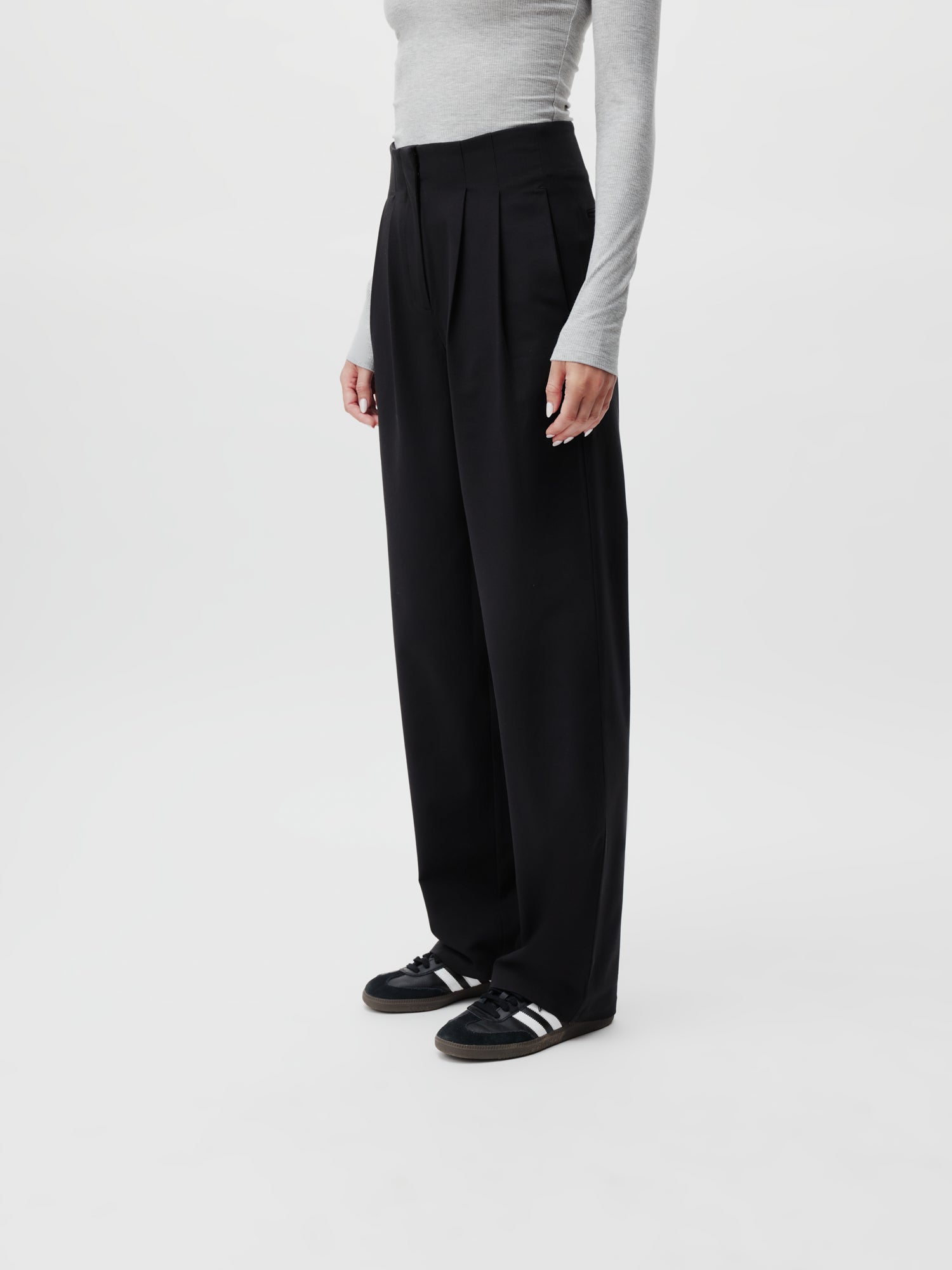 Eine Person ist gestylt in einem hellgrauen Langarmshirt kombiniert mit der Marla Pants Tall von LeGer by Lena Gercke, mit hoch tailliertem, weitem Bein in Größe 38. Ergänzt wird das Outfit durch schwarze Sneakers mit weißen Streifen für einen schnittigen Auftritt. Der schlichte weiße Hintergrund bleibt einheitlich.