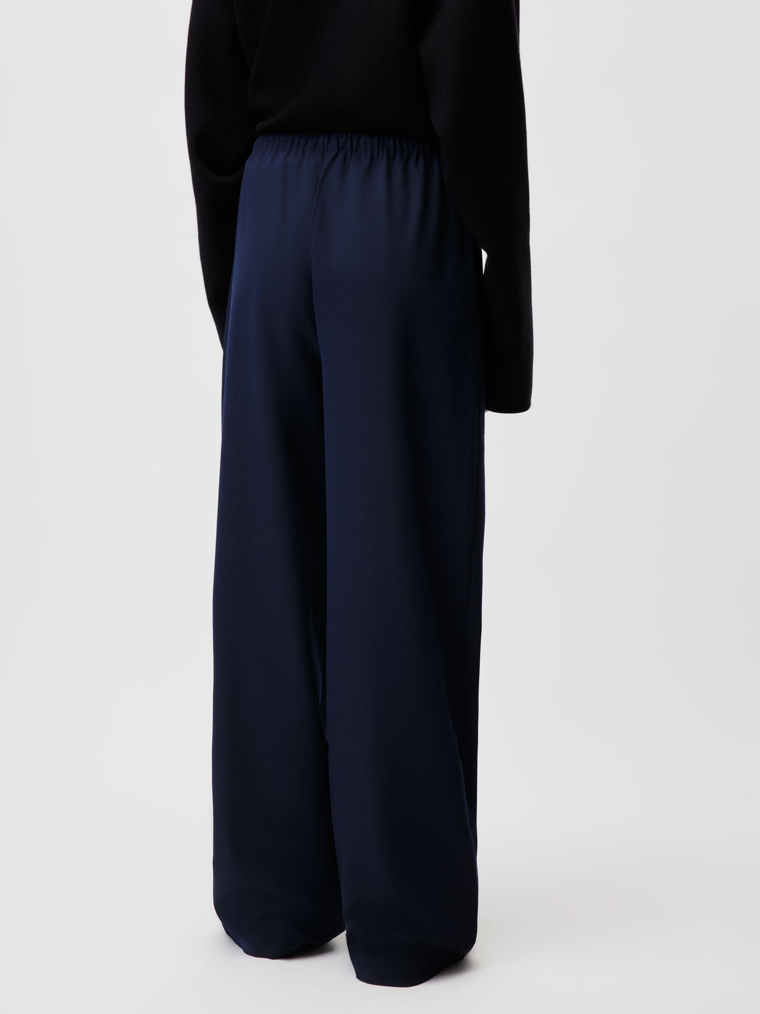 Ein Model in Größe 36 in einem schwarzen Top und LeGer by Lena Gercke Kim Pants in Marineblau steht mit dem Rücken zur Kamera vor einem schlichten hellen Hintergrund.