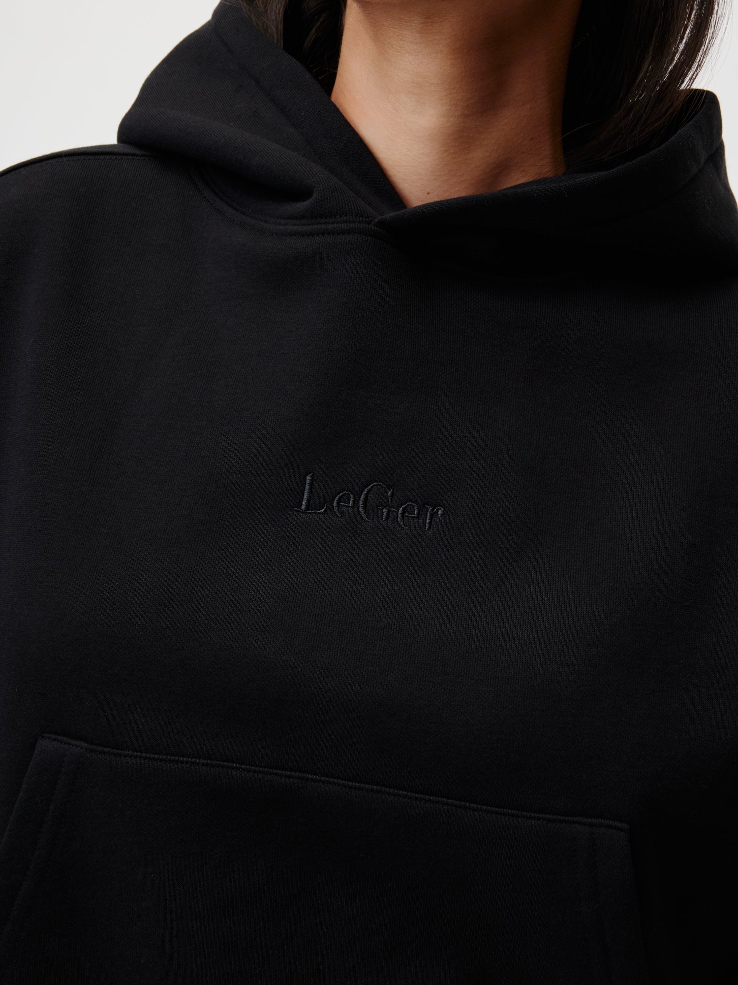 Eine Nahaufnahme zeigt jemanden, der den Cybil Hoodie von LeGer by Lena Gercke trägt. Auf der Brust ist der dezent gestickte „LeGer“-Schriftzug zu sehen, und das Langarmdesign mit normaler Länge hebt die modischen Elemente des Hoodies hervor und lässt das Gesicht der Person unsichtbar.