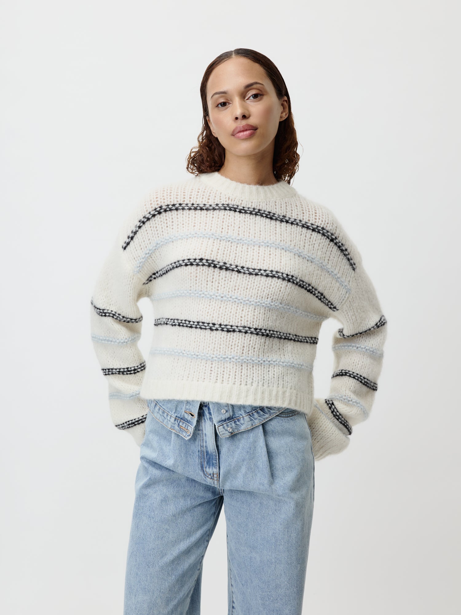 Eine Person steht selbstbewusst da, gekleidet in einen gemütlichen, übergroßen Paulina-Pullover von LeGer by Lena Gercke mit schwarz-weißen Querstreifen, kombiniert mit hellblauen Jeans. Der schlichte weiße Hintergrund verstärkt den entspannten Locker-Vibe des Outfits und behält gleichzeitig eine normale Länge bei, die den Look mühelos ergänzt.