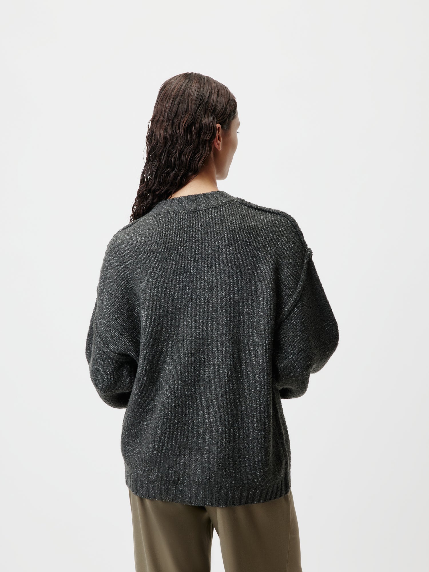 Rückansicht einer Person mit langen, welligen Haaren, die den Pullover Elsa von LeGer by Lena Gercke mit Langarm in dunkelgrauem, übergroßem Design trägt. Sie steht vor einem schlichten, hellen Hintergrund und trägt olivgrüne Hosen.