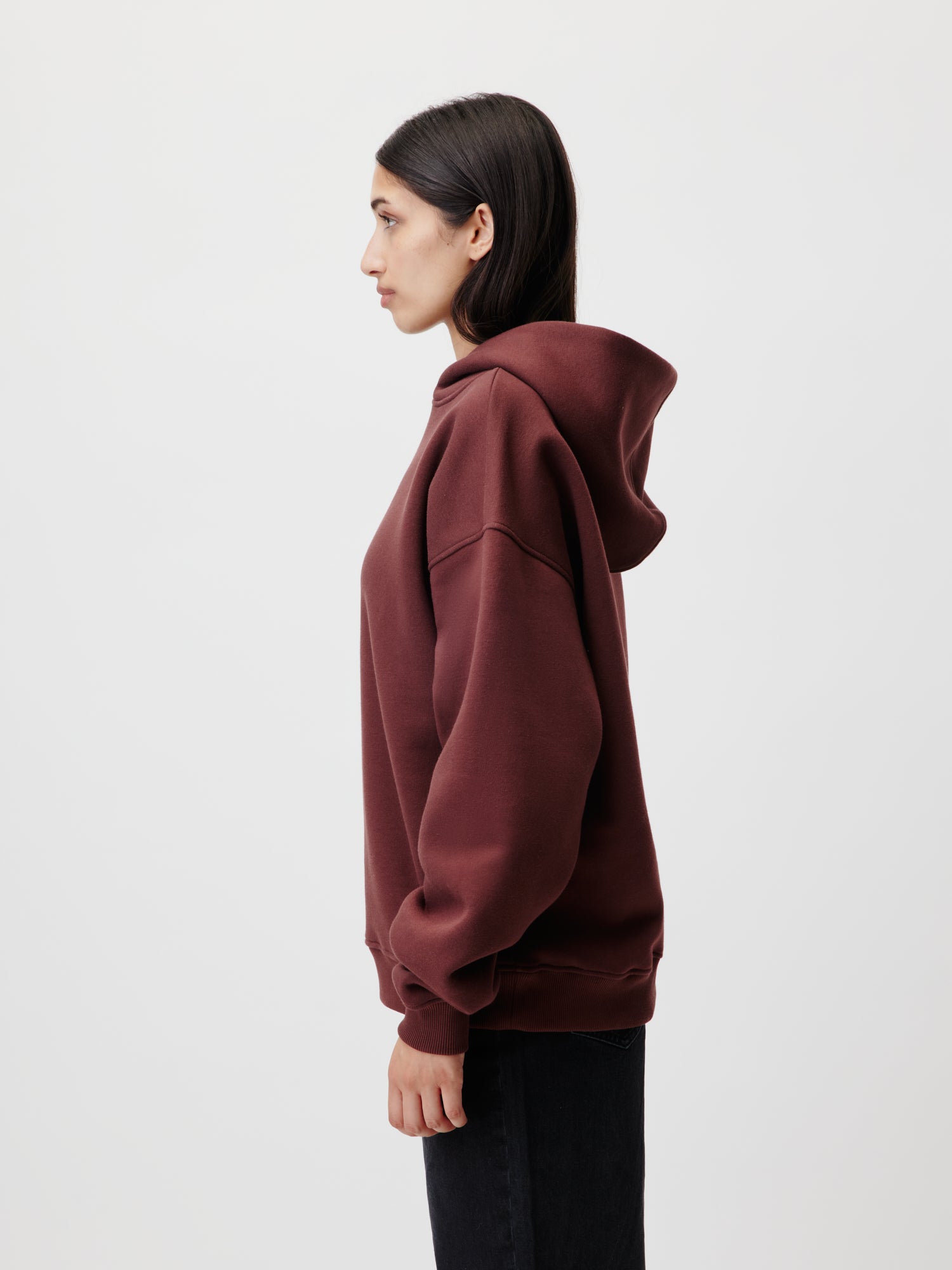 Eine Person mit langen dunklen Haaren steht im Profil vor einem weißen Hintergrund und trägt einen dunkelroten Abby Hoodie von LeGer by Lena Gercke mit langen Ärmeln und eine schwarze Hose, alles in Größe 36.