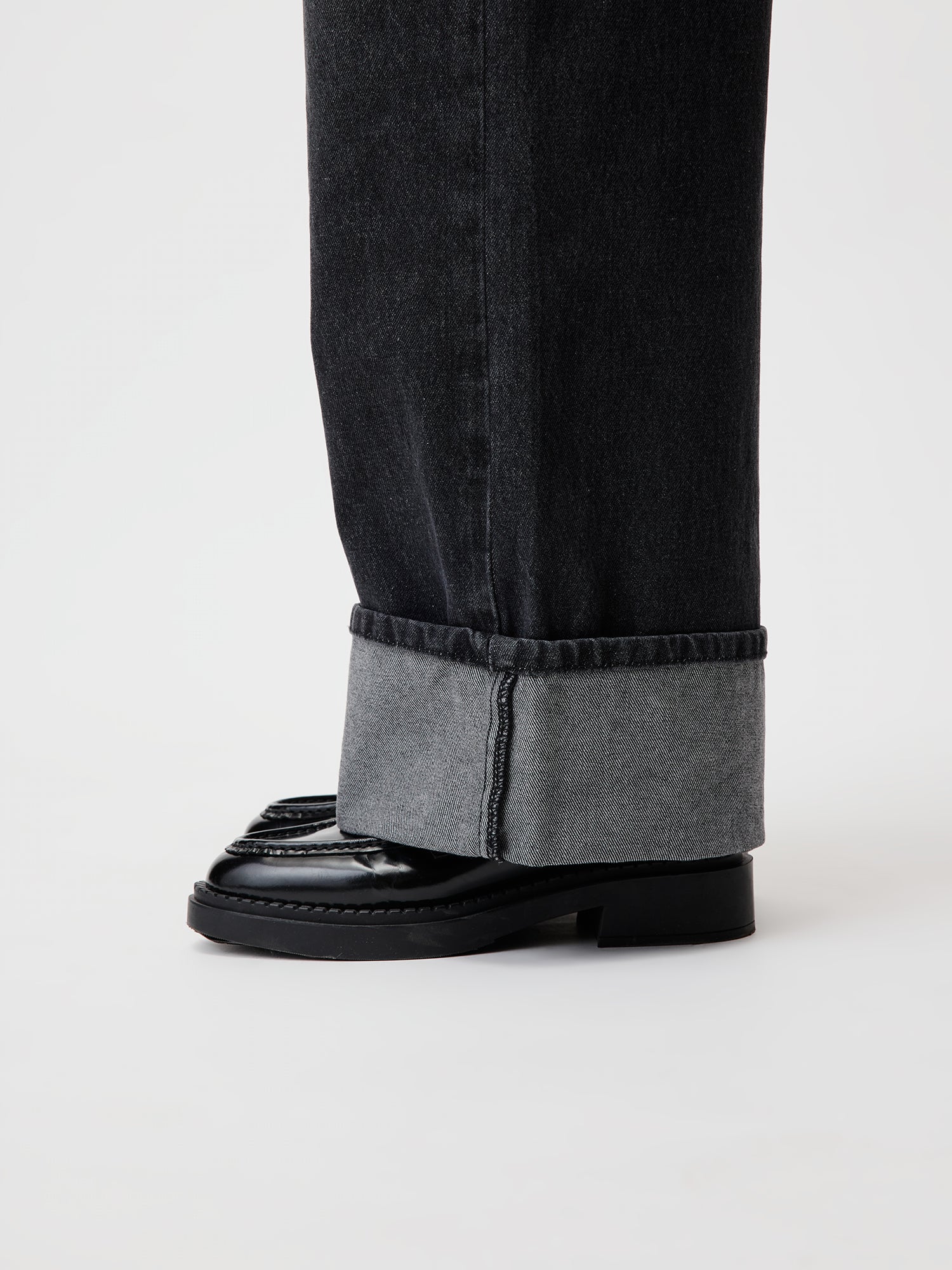 Nahaufnahme der Marin-Hose von LeGer by Lena Gercke, die ihre breiten Bündchen zeigt und einen Teil eines schwarzen, glänzenden Slipper zeigt. Die Hose hat ein helles Innenfutter, das mit dem dunkleren Stoff kontrastiert. Der Schuh hat eine dicke Sohle und auffällige Nähte an der Spitze, die diesem Lang/Maxi-Stil Flair verleihen.