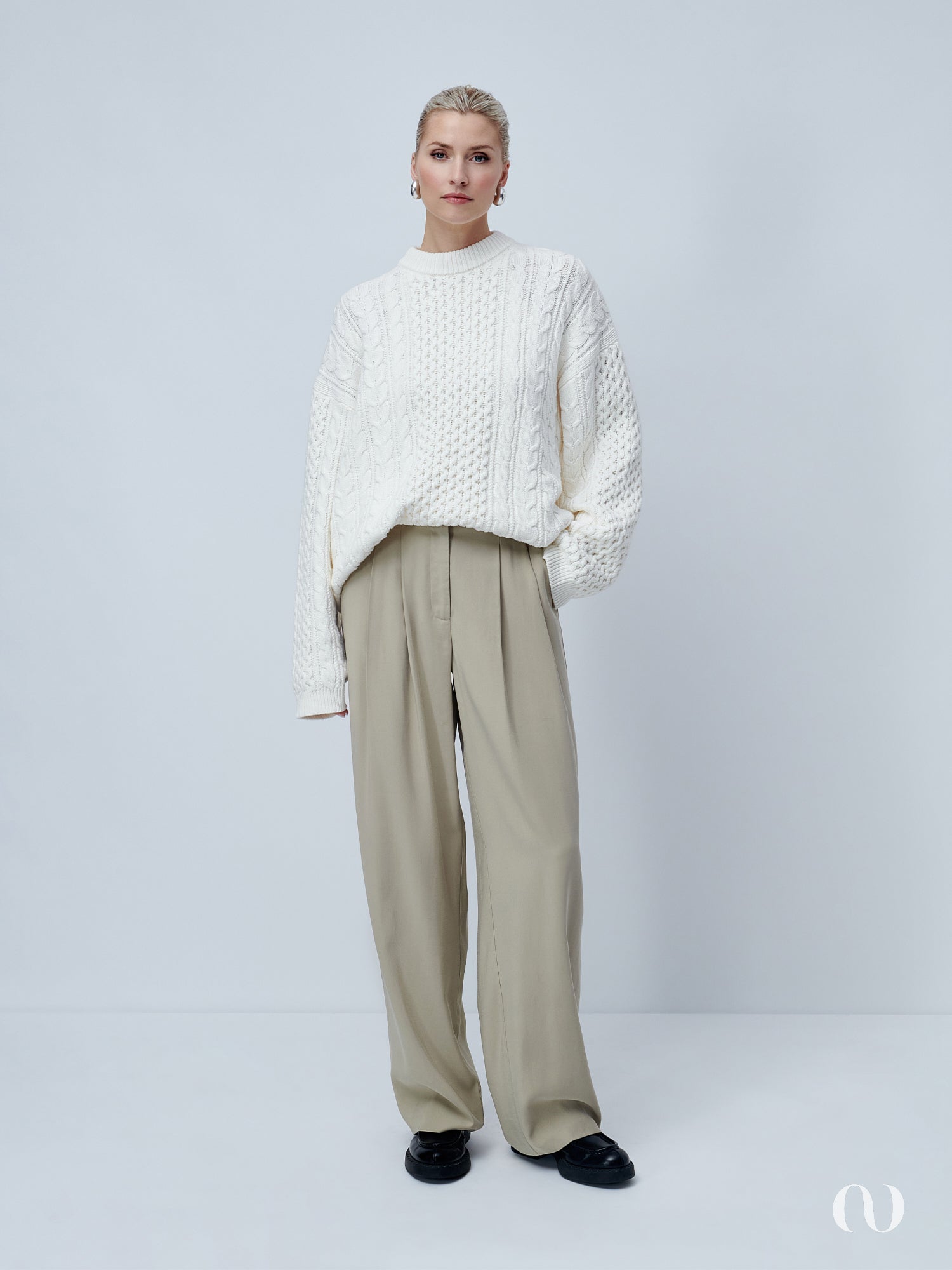 Eine Person steht vor einem schlichten Hintergrund und trägt einen übergroßen weißen Danika-Pullover von LeGer by Lena Gercke und beige Hosen mit weitem Bein, kombiniert mit schwarzen Schuhen. Der Gesamtstil ist minimalistisch und schick.